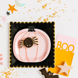 A cute Halloween or Fall table set up. A pink 7 inch pumpkin shaped plate sits on top of a black square plate with scalloped edges. On top of the plate is a cute spider shaped cookie with a bat shaped cookie.