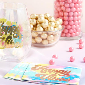 Tie die napkins with gold letters reading Happy Vibes and pink candy around it.