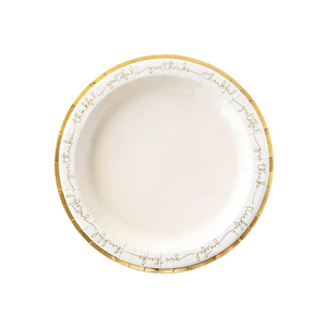 A white plate with gold edges and script words that reads thankful and grateful lays on a white background.