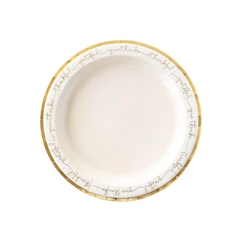 A white plate with gold edges and script words that reads thankful and grateful lays on a white background.