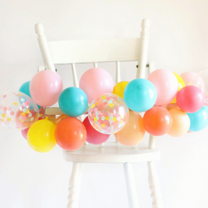 DIY mini balloon garland with multiple colors wrapped on a white kids high chair.