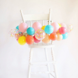 Mini balloon garland wrapped around a white high chair.