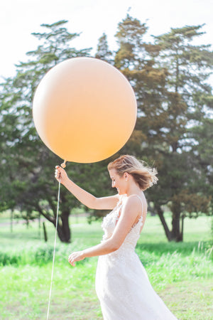 Girl in white dress holding a jumbo 36 inch balloon in a blush color.