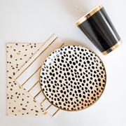 Black dot cream colored plates next to a black paper cup with gold rim.