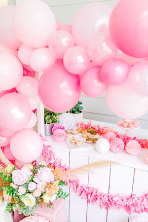 A side angle of the stand shows a pretty pink rug with a floral balloon and light pink pillows resting up against the stand that the balloon garland is on.