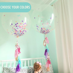 Toddler sitting on a bed with two 3ft clear balloon stuffed with tissue confetti and tassel string.