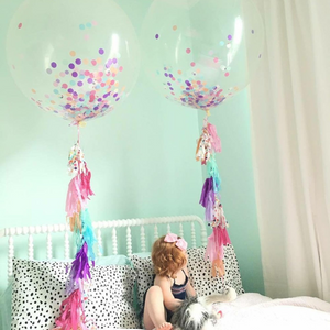 Toddler sitting on a bed with two 3ft clear balloon stuffed with tissue confetti and tassel string.