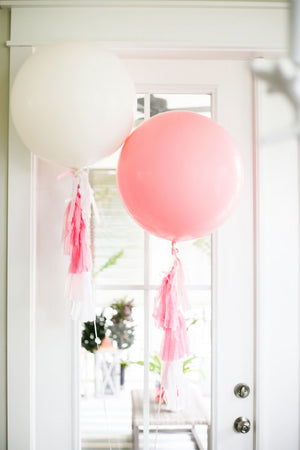 Two jumbo 36 inch balloons are floating in front of a white glass door. One is pink and the other is a white balloon.