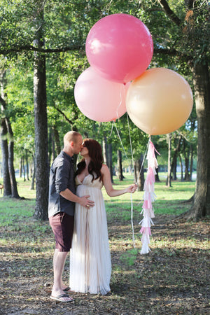 Couple kissing and holding three jumbo balloons one is rose colored.