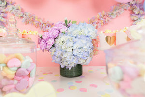 Pile of pastel colored hand cut tissue confetti paper on a pink table with a pastel flower arrangement.