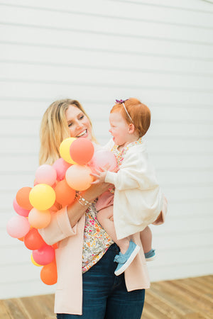 Woman holds a baby girl and a mini balloon garland.