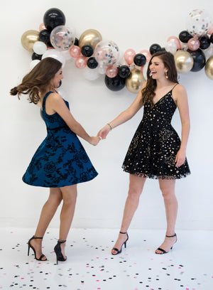 Two girls wearing dresses dance on top of the confetti while looking at each other laughing.