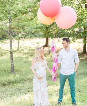 A couple looking at each other smiling and holding three jumbo balloons.