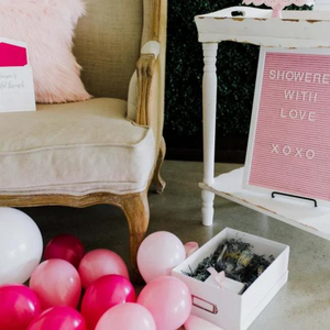 Various inflated pink and white 5 inch balloons scattered on the ground next to a tan colored chair and white side table.