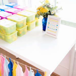 Close up of hand rolled tissue tassels in the colors pink, blue, and yellow hanging from a white table.
