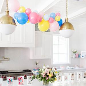 A 4ft assortment of pink, blue, and yellow balloons hangs above a white kitchen island.
