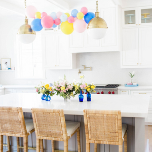 A mini 4ft balloon garland with the colors pink, blue, and yellow hangs above a white kitchen island.