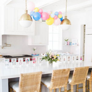 A pink, yellow, and blue balloon garland hangs above a white kitchen island for a little girls birthday celebration.
