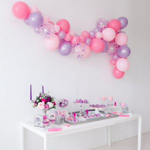 Pink and purple balloon garland beautifully hung above a white table full of pink and purple sweets and treats.