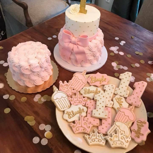 A platter full of cookies and a cake sit on a dark wooden table with gold, mauve, and pink tissue confetti spread around.