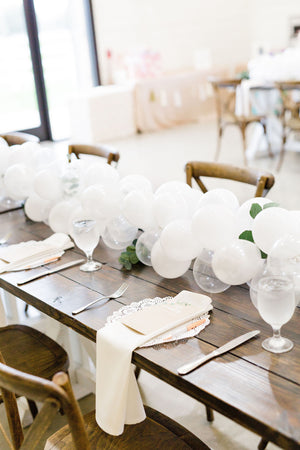 Close up of a 20 foot white balloon garland with an assortment of 5 inch pearl white, white, and clear balloons sits as a centerpiece on a rustic wood table.