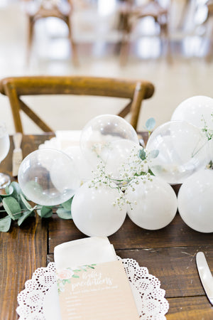 Close up of 20 foot white balloon garland with an assortment of 5 inch pearl white, white, and clear balloons sits as a centerpiece on a rustic wood table.