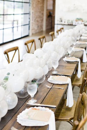 20 foot white balloon garland with an assortment of 5 inch pearl white, white, and clear balloons sits as a centerpiece on a rustic wood table.