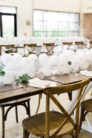 Close up of 20 foot white balloon garland with an assortment of 5 inch pearl white, white, and clear balloons sits as a centerpiece on a rustic wood table. Perfect for a bridal shower, wedding shower, boho baby shower, or wedding.