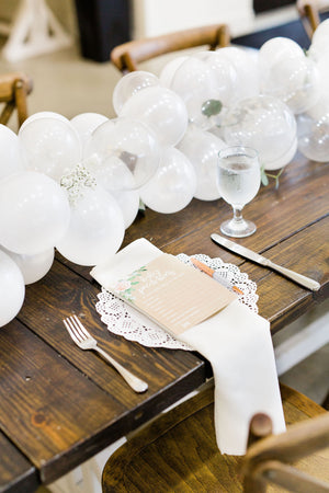 Close up of 20 foot white balloon garland with an assortment of 5 inch pearl white, white, and clear balloons sits as a centerpiece on a rustic wood table. Perfect for a bridal shower, wedding shower, boho baby shower, or wedding.