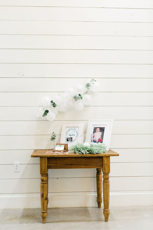 Close up of 20 foot white balloon garland with an assortment of 5 inch pearl white, white, and clear balloons sits as a centerpiece on a rustic wood table. Perfect for a bridal shower, wedding shower, boho baby shower, or wedding.