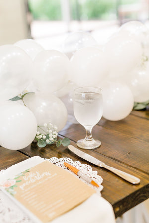 Close up of 20 foot white balloon garland with an assortment of 5 inch pearl white, white, and clear balloons sits as a centerpiece on a rustic wood table. Perfect for a bridal shower, wedding shower, boho baby shower, or wedding.