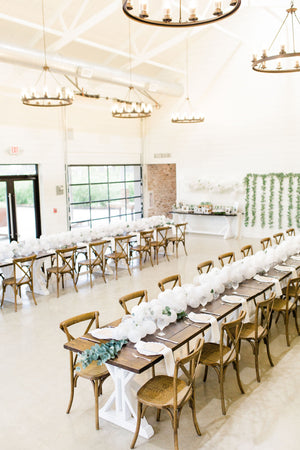 A 20 foot white balloon garland with an assortment of 5 inch pearl white, white, and clear balloons sits as a centerpiece on a rustic wood table. Perfect for a bridal shower, wedding shower, boho baby shower, or wedding.