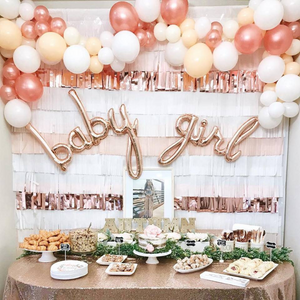 A baby girl baby shower with rose gold script BABY GIRL balloons on the backdrop.