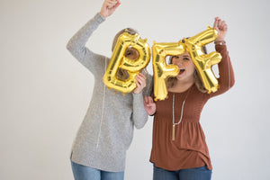 Two girls now hide behind the letter balloons while holding them up in front of their faces.