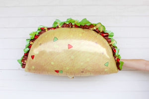 Hand holding the back of a 33 inch jumbo taco balloon. The taco balloon has a light brown shell with toppings on top.