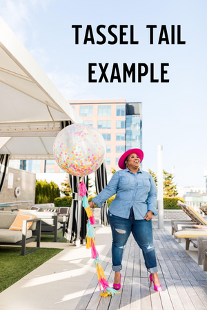 Woman holding a clear balloon filled with confetti with matching tassel tail on the balloon.