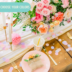 An arial shot shows soft pink, lilac, and blush one inch circular tissue confetti spread all over a wooden table with a pretty bouquet of flowers sitting in the middle.