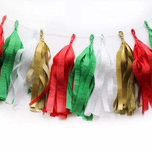 An arial shot of a Christmas themed tissue tassel garland sitting on a white table made up of red, green, white, and gold.