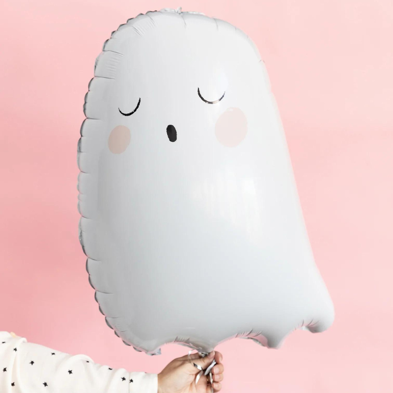 Womans hand holding a 26 inch tall cute ghost balloon. There is a pink wall in the background.