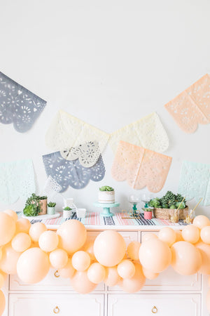A blush balloon garland hangs from a white dresser. On top of the dresser is a white cake.