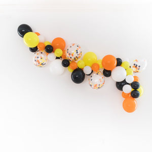 A straight on view of the balloon garland on a white wall. With the colors shown of orange, white, black, and yellow. As well as a few 11 inch clear confetti filled matching balloons.