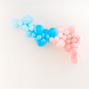 A soft pretty balloon garland is draped on a white wall. With a mix of pastel light blue, light blue, pastel pink, and pink balloons in that order from left to right.