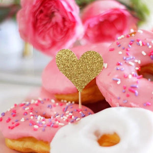 Gold glitter heart toppers on a pink donut with sprinkles.