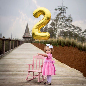 A little girl standing on a bridge with a gold number 2 floating behind her.