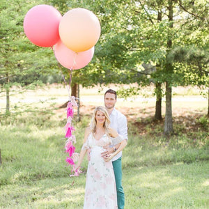 Couple holding three jumbo 36 inch balloons in the colors rose, blush, and pink with a string tassel in different shades of pink.