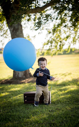 Little boy smiling holding a light blue jumbo 36 inch balloon at the park.