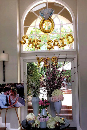 Engagement party decorations inside a home with a jumbo gold diamond ring balloon and jumbo gold letters spelling SHE SAID YES.