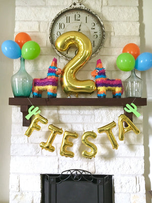 Gold letter balloons spelling FIESTA hung on a white brick chimney below a gold number two #2 balloon.
