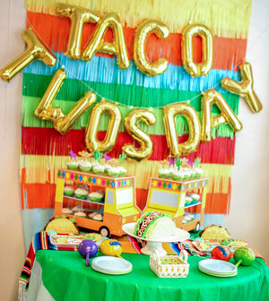 Gold mylar letter balloons spelling TACO TWOSDAY used in celebration of two year old birthday party in a taco fiesta themed party.