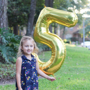 A jumbo 5 balloon as big the little girl holding it.